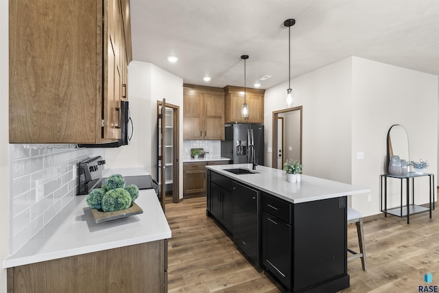 kitchen featuring light countertops, brown cabinetry, a sink, light wood-type flooring, and black appliances