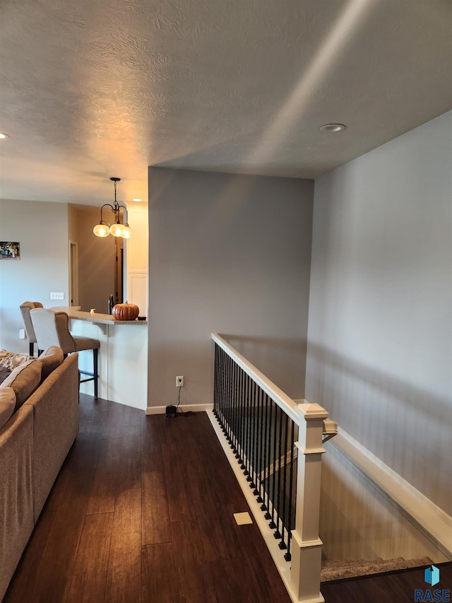 corridor featuring an inviting chandelier, a textured ceiling, and dark wood-type flooring