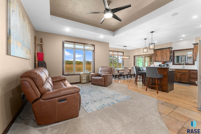 living room featuring ceiling fan, sink, a raised ceiling, and light hardwood / wood-style flooring