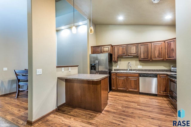 kitchen featuring hanging light fixtures, sink, kitchen peninsula, wood-type flooring, and stainless steel appliances