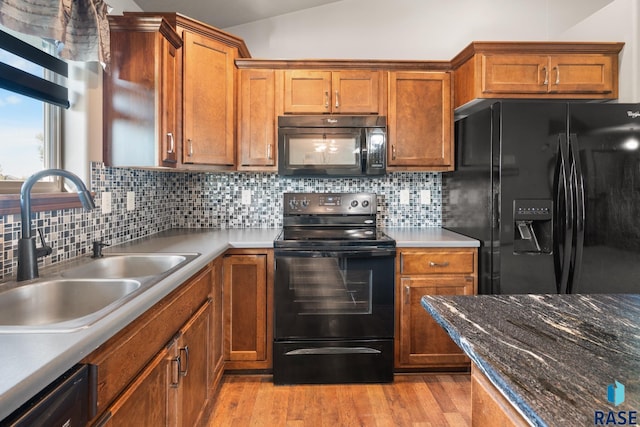 kitchen featuring light wood-type flooring, backsplash, vaulted ceiling, and black appliances