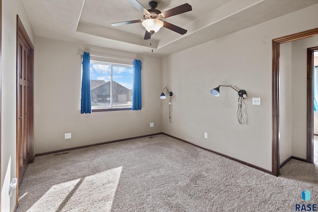 unfurnished bedroom featuring light carpet, ceiling fan, and a tray ceiling