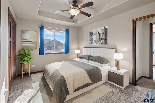 bedroom with ceiling fan, a tray ceiling, and light colored carpet