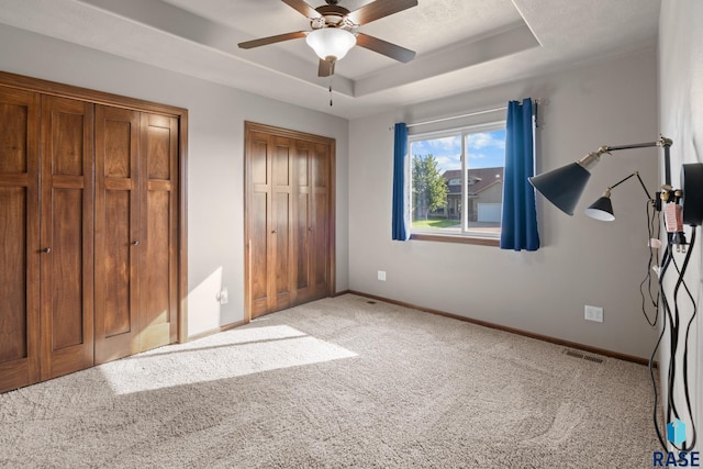 unfurnished bedroom featuring light carpet, ceiling fan, and a raised ceiling