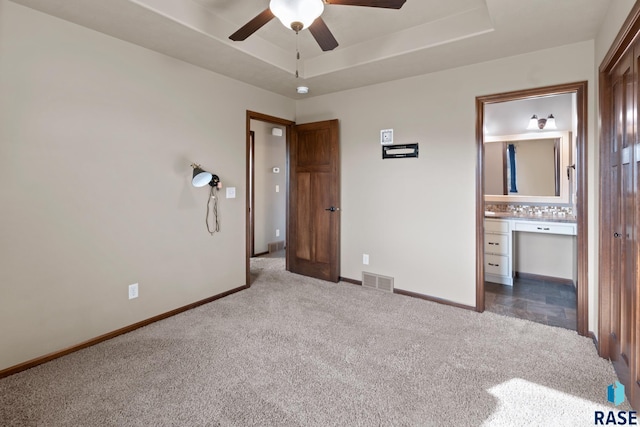 unfurnished bedroom with ceiling fan, ensuite bath, a raised ceiling, and light colored carpet