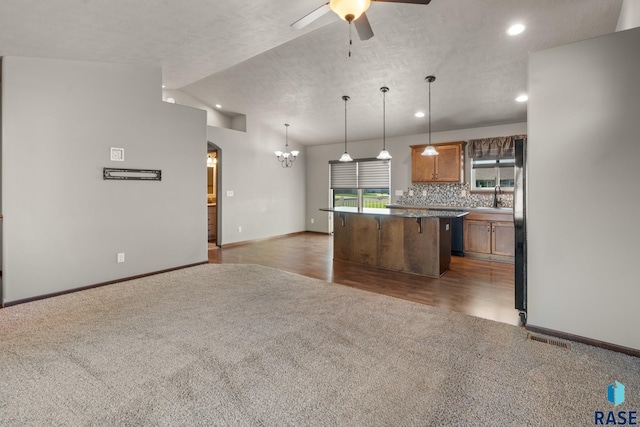 kitchen with a textured ceiling, ceiling fan with notable chandelier, a kitchen bar, and dark hardwood / wood-style flooring