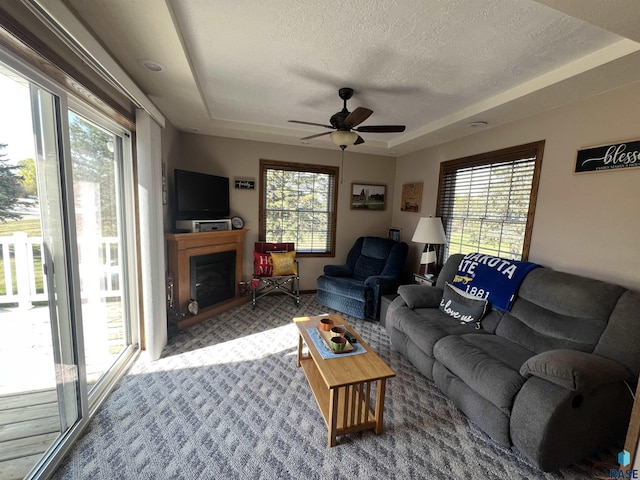 1495 115th St, Luverne, MN 56156 - living room with carpet, ceiling fan, a textured ceiling, a tray ceiling, and a fireplace with raised hearth