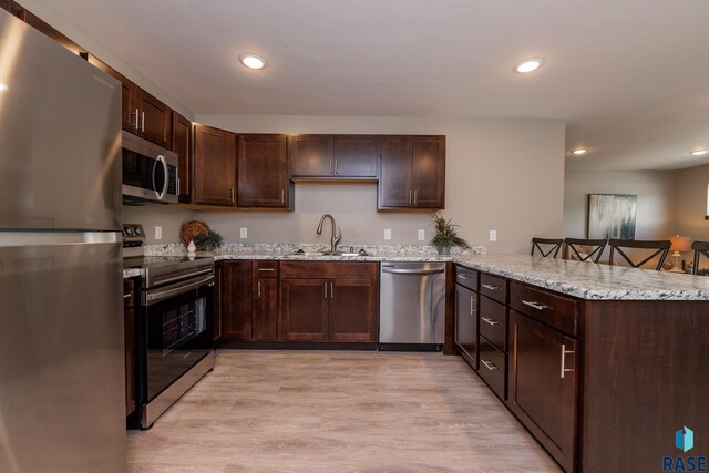 kitchen featuring appliances with stainless steel finishes, kitchen peninsula, sink, and light wood-type flooring