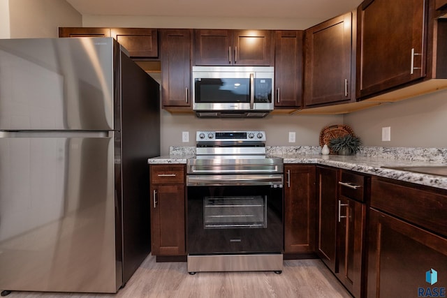 kitchen featuring dark brown cabinetry, light stone countertops, appliances with stainless steel finishes, and light hardwood / wood-style flooring