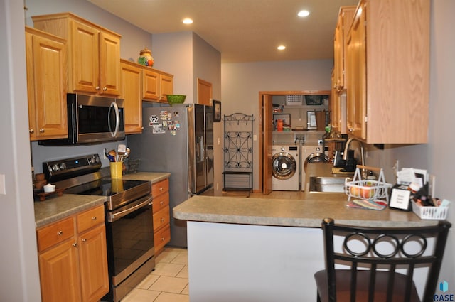 kitchen with a kitchen breakfast bar, sink, kitchen peninsula, washing machine and dryer, and appliances with stainless steel finishes