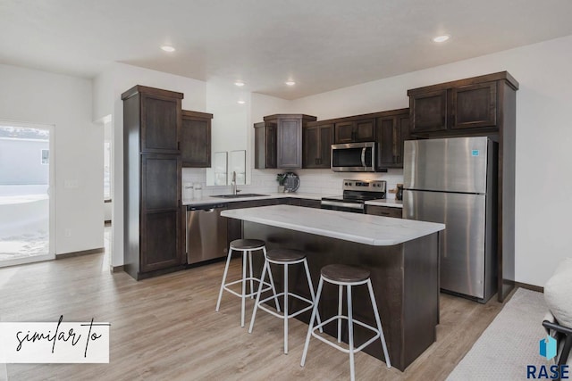 kitchen featuring sink, a center island, stainless steel appliances, a breakfast bar, and light wood-type flooring