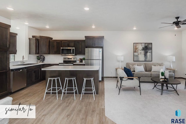 kitchen with light wood-type flooring, a kitchen breakfast bar, sink, appliances with stainless steel finishes, and a center island