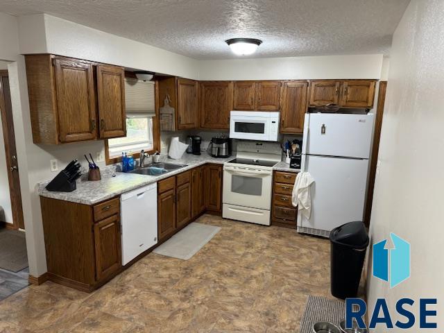 kitchen featuring a textured ceiling, white appliances, and sink