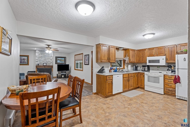 kitchen featuring white appliances, a stone fireplace, sink, ceiling fan, and a textured ceiling