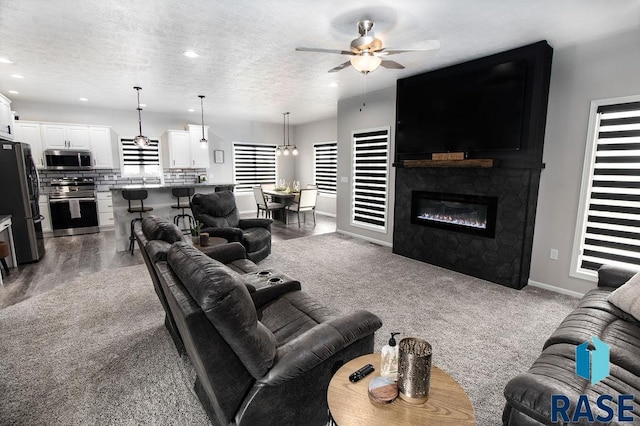 living room featuring a textured ceiling, ceiling fan, a stone fireplace, and carpet