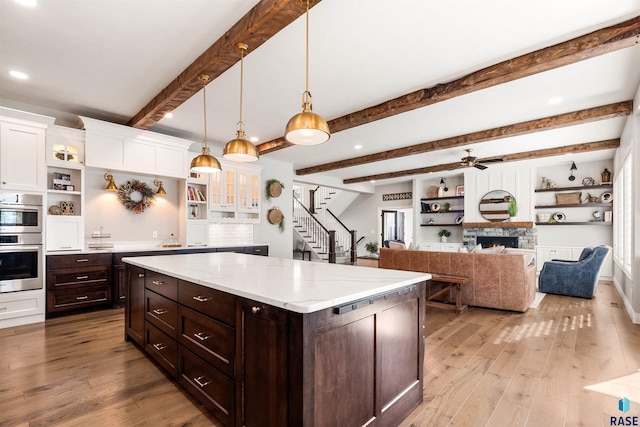 kitchen with light hardwood / wood-style floors, beamed ceiling, decorative light fixtures, and stainless steel double oven