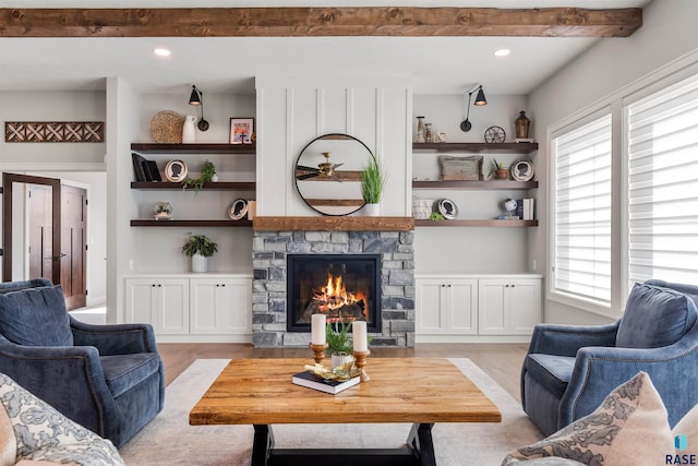 living room with a stone fireplace, beam ceiling, and light hardwood / wood-style floors