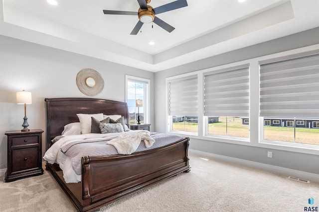 bedroom featuring ceiling fan, a tray ceiling, multiple windows, and light colored carpet