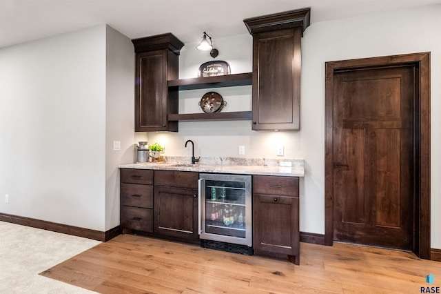 bar with dark brown cabinetry, light wood-type flooring, and beverage cooler