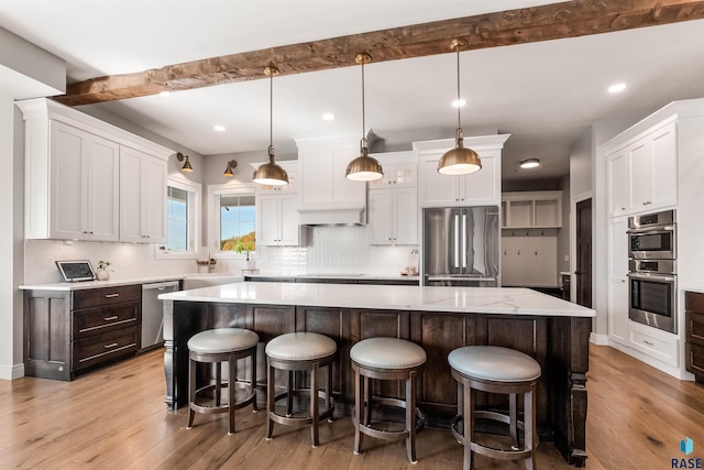 kitchen with a kitchen island, light hardwood / wood-style flooring, decorative light fixtures, white cabinetry, and appliances with stainless steel finishes