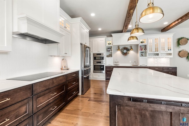 kitchen with tasteful backsplash, appliances with stainless steel finishes, hanging light fixtures, beam ceiling, and light hardwood / wood-style flooring