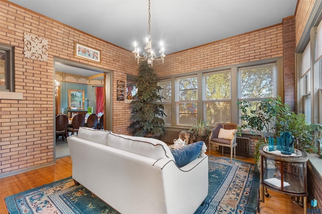 living room with light hardwood / wood-style floors, a notable chandelier, and brick wall