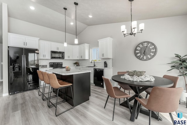 kitchen with hanging light fixtures, a kitchen island, white cabinetry, black appliances, and sink