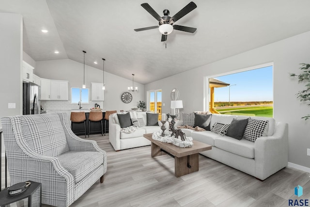 living room featuring light hardwood / wood-style floors, lofted ceiling, ceiling fan with notable chandelier, and a wealth of natural light