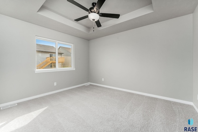 carpeted empty room featuring ceiling fan and a raised ceiling