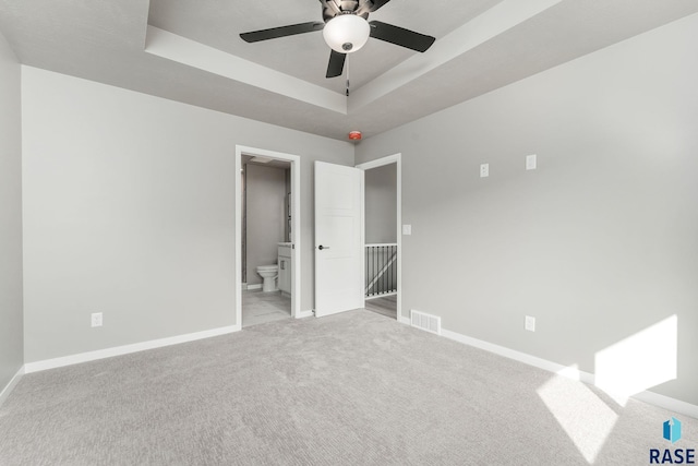 unfurnished bedroom with light carpet, ensuite bathroom, a raised ceiling, and ceiling fan