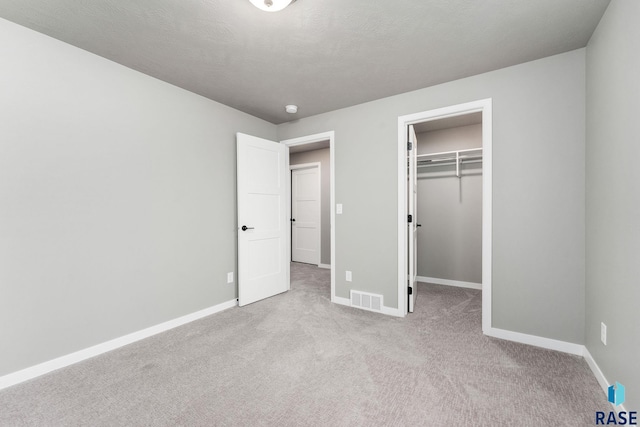 unfurnished bedroom with a closet, light carpet, a textured ceiling, and a walk in closet