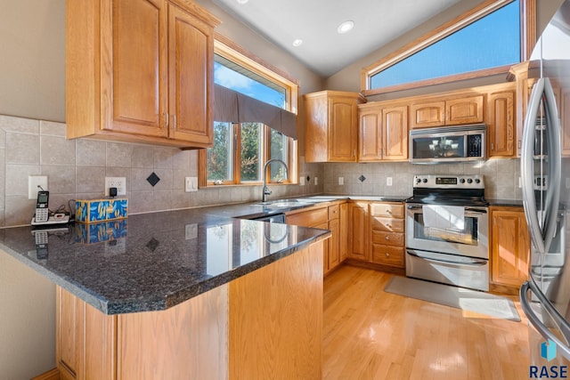 kitchen featuring light hardwood / wood-style flooring, kitchen peninsula, dark stone counters, sink, and appliances with stainless steel finishes