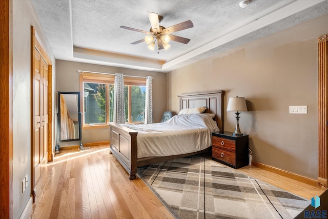 bedroom featuring ceiling fan, a tray ceiling, a textured ceiling, and light hardwood / wood-style flooring