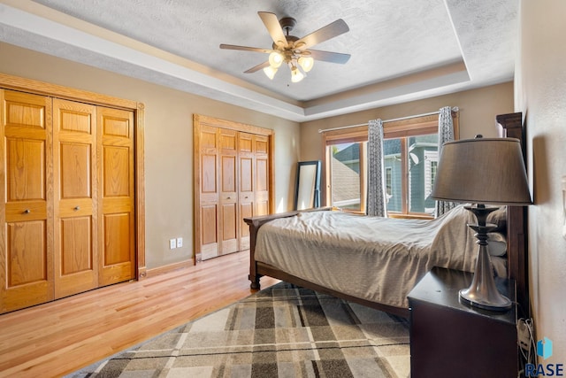 bedroom with multiple closets, hardwood / wood-style floors, a raised ceiling, a textured ceiling, and ceiling fan