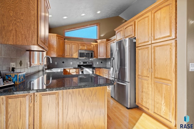 kitchen featuring kitchen peninsula, decorative backsplash, lofted ceiling, appliances with stainless steel finishes, and light hardwood / wood-style flooring