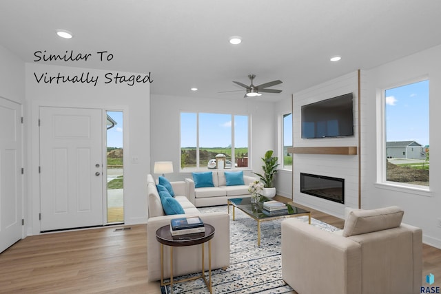 living room with ceiling fan, a large fireplace, and light wood-type flooring