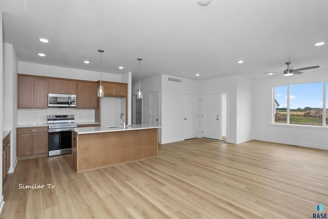 kitchen featuring ceiling fan, hanging light fixtures, stainless steel appliances, light hardwood / wood-style flooring, and a kitchen island with sink