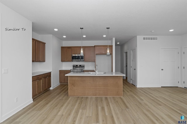 kitchen featuring sink, light hardwood / wood-style floors, decorative light fixtures, a kitchen island with sink, and appliances with stainless steel finishes