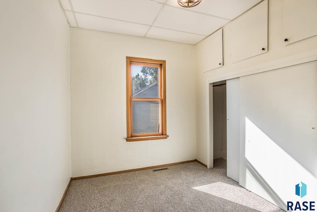 unfurnished bedroom with a closet, light colored carpet, and a drop ceiling