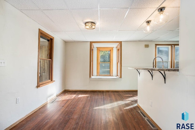 unfurnished room featuring a drop ceiling, dark wood-type flooring, and plenty of natural light