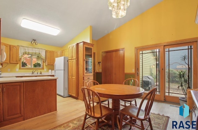 dining area with light hardwood / wood-style floors, a notable chandelier, and vaulted ceiling