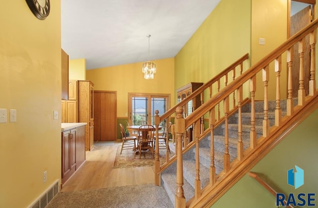 stairs featuring an inviting chandelier, lofted ceiling, and hardwood / wood-style flooring