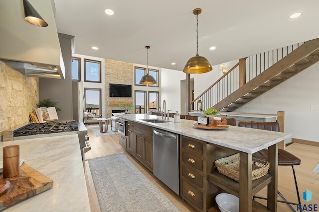 kitchen with dishwasher, a stone fireplace, sink, light stone countertops, and pendant lighting