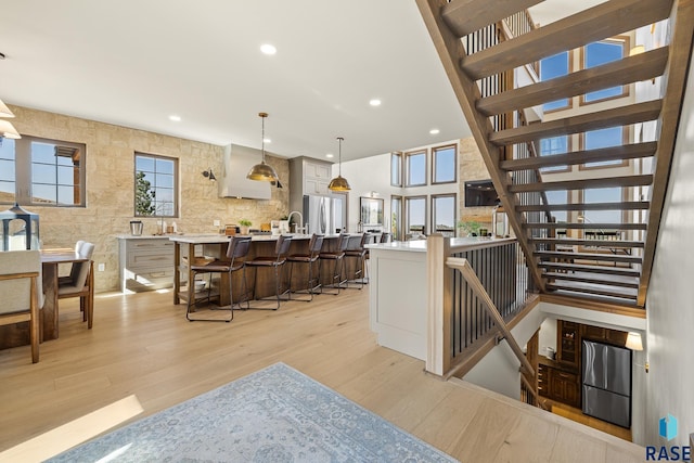 kitchen with a breakfast bar, stainless steel fridge, decorative light fixtures, and light wood-type flooring