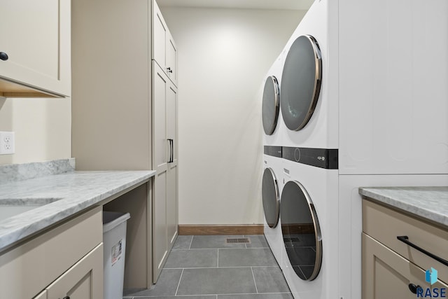 laundry room featuring dark tile patterned flooring, cabinets, and stacked washer and dryer