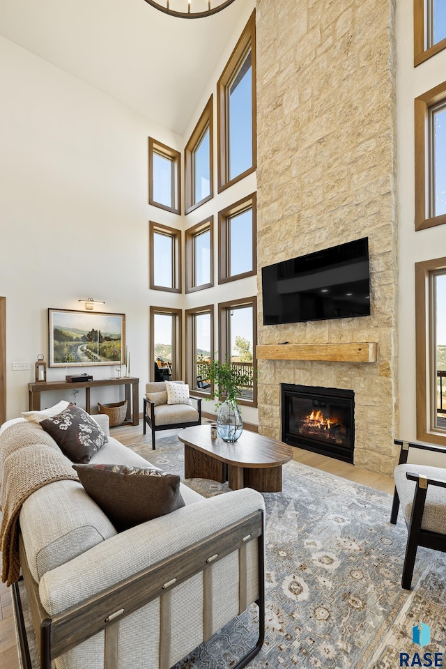 living room with a healthy amount of sunlight, a stone fireplace, and a towering ceiling