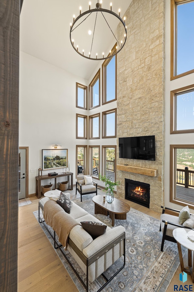 living room featuring a stone fireplace, a notable chandelier, high vaulted ceiling, and light wood-type flooring