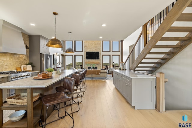 kitchen featuring hanging light fixtures, a spacious island, premium range hood, gray cabinets, and stainless steel appliances