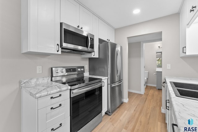 kitchen with white cabinets, light stone counters, stainless steel appliances, and light hardwood / wood-style floors