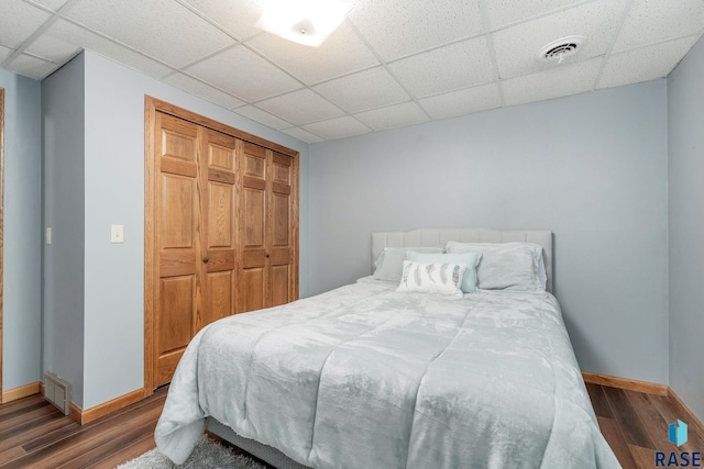 bedroom with a closet, a paneled ceiling, and dark hardwood / wood-style flooring